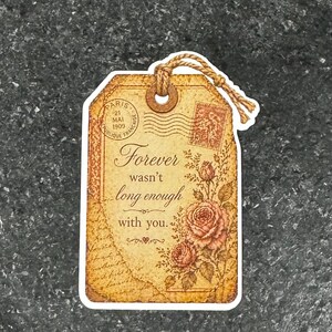 May include: A vintage-style gift tag with a brown paper texture, featuring the text "Forever wasn't long enough with you." It includes a floral design with roses and a postage stamp illustration. A twine loop is attached.
