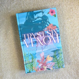 May include: A hardback book titled Tryst Six Venom by Penelope Douglas. The cover features a person on a motorcycle, a pink hibiscus flower, a small octopus, and green seaweed illustrations over a blue ocean background with white text.
