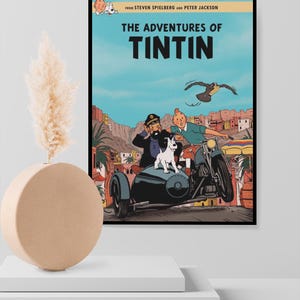 May include: A framed movie poster for The Adventures of Tintin featuring Tintin, Captain Haddock, and Snowy riding a motorcycle with a sidecar through a desert town. The text reads From Steven Spielberg and Peter Jackson The Adventures of Tintin.