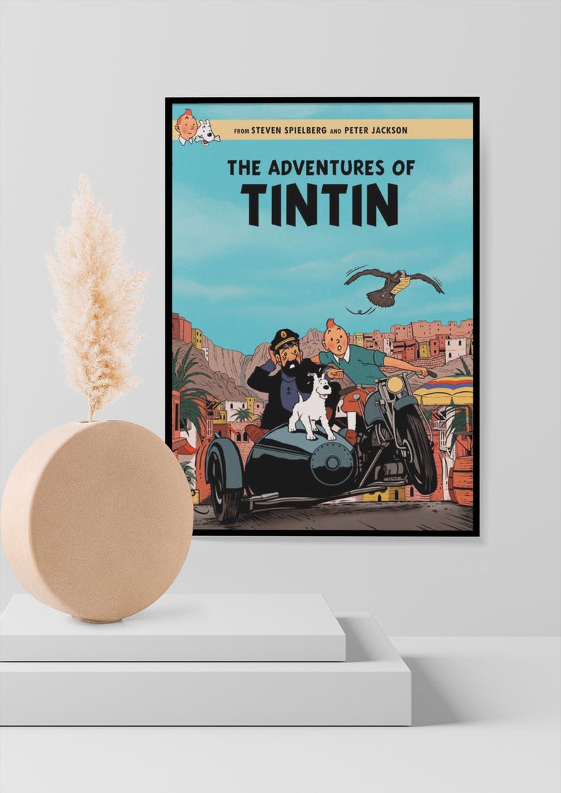 May include: A framed movie poster for The Adventures of Tintin featuring Tintin, Captain Haddock, and Snowy riding a motorcycle with a sidecar through a desert town. The text reads From Steven Spielberg and Peter Jackson The Adventures of Tintin.