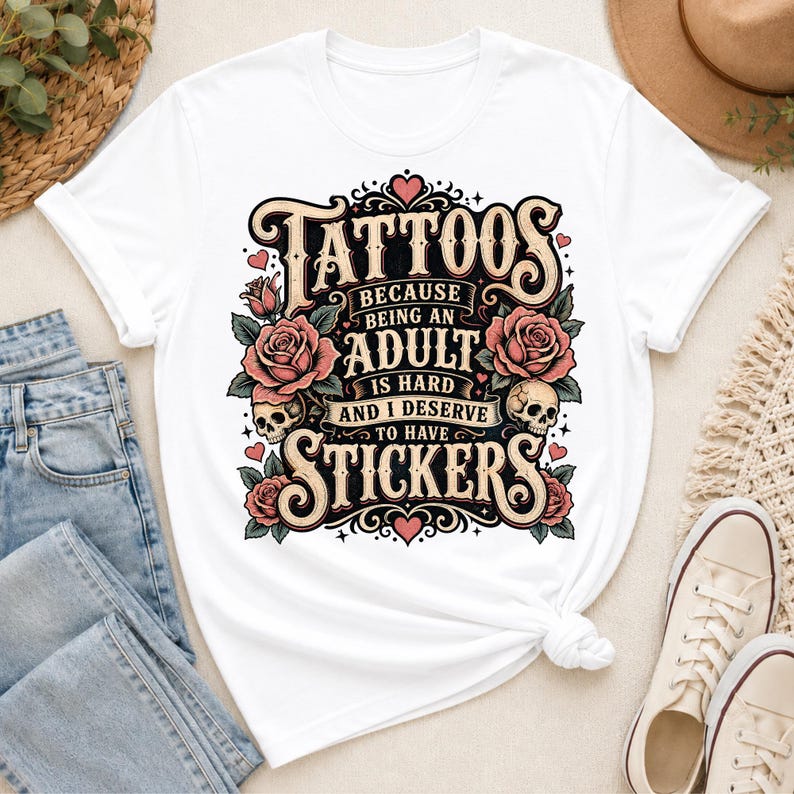 May include: White t-shirt featuring a graphic design with the words "Tattoos" and "Stickers." The design includes roses, skulls, and the phrase "Because being an adult is hard and I deserve to have." The shirt is knotted at the waist.