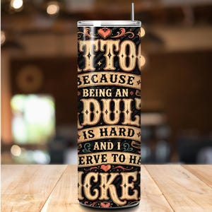 K&ouml;nnte beinhalten: Ein schwarz-becher mit Strohhalm, mit dem Text "Tattoos because being an adult is hard and I deserve to have cake." Der Text ist in einer Vintage-Schrift mit Herzakzenten gehalten. Der Becher steht auf einer Holzoberfl&auml;che.
