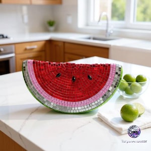 Könnte beinhalten: Eine halbmondförmige Wassermelonenskulptur aus kleinen Mosaikfliesen in den Farben Rot, Rosa, Grün und Silber. Das Objekt weist schwarze, ovale Akzente auf, die Kerne darstellen, und ist in einem geschwungenen, segmentierten Muster angeordnet.