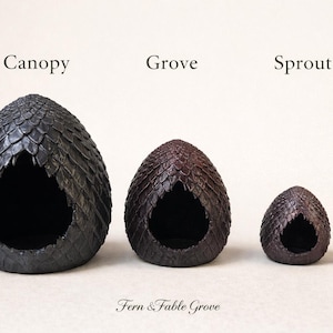 May include: Three decorative, egg-shaped structures with textured exteriors, labelled "Canopy", "Grove", and "Sprout". A small, clear glass object is next to the smallest egg. The text "Fern & Fable Grove" is at the bottom.