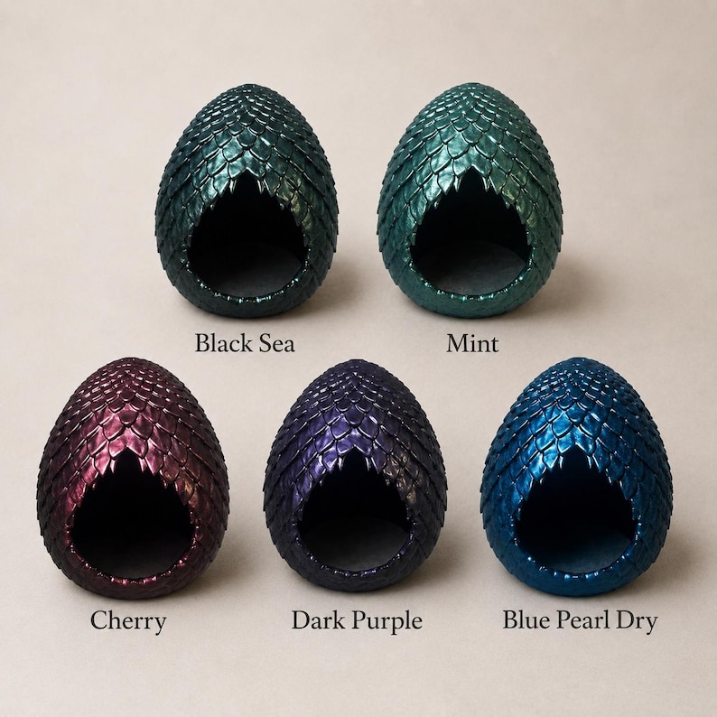 Op de afbeelding: Vijf eivormige houders met een gestructureerd schubpatroon. De kleuren zijn gelabeld als Black Sea, Mint, Cherry, Dark Purple en Blue Pearl Dry. Elk object heeft een grote, uitgeholde opening aan de voorzijde die een gladde binnenkant onthult.