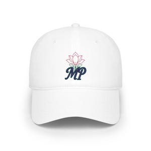 May include: A white baseball cap featuring an embroidered design on the front. The design consists of a pink outlined flower with green leaves positioned above the dark blue embroidered letters MP in a cursive script font style.