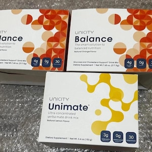 Puede incluir: Tres cajas de suplementos dietéticos Unicity. Dos cajas están etiquetadas como "Balance" con diseños naranjas y blancos, y la tercera es "Unimate" con diseños amarillos y blancos. Las cajas "Balance" indican "Natural Orange Flavor". La caja "Unimate" indica "Natural Lemon Flavor".