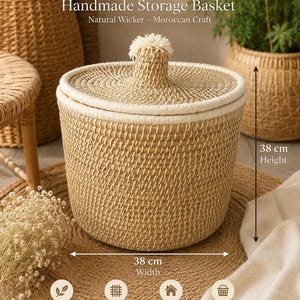 May include: A cylindrical handmade storage basket crafted from natural wicker with a matching lid featuring a central knob. The basket has a height of 38 cm and a width of 38 cm. The text "Handmade Storage Basket" and "Natural Wicker - Moroccan Craft" is visible.