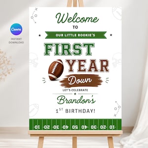 May include: A white rectangular sign featuring green and brown text that reads Welcome to our little rookie's first year down, let's celebrate Brandon's 1st birthday. The design includes a brown football graphic and a green football field border.
