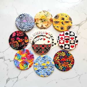 Puede incluir: Una colección de nueve tarjeteros circulares de tela con varios patrones, incluyendo girasoles, rosas, estampados florales y palos de cartas. Un tarjetero está abierto y contiene un abanico de cartas de juego estándar con números y palos.