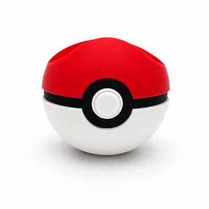 Puede incluir: Un contenedor rojo, blanco y negro con forma de Pok&eacute; Ball. La mitad superior es roja, la mitad inferior es blanca, y una banda negra con un bot&oacute;n blanco detalla el centro. El contenedor tiene dos aberturas en la parte superior.