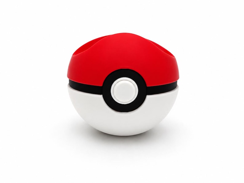 Puede incluir: Un contenedor rojo, blanco y negro con forma de Pok&eacute; Ball. La mitad superior es roja, la mitad inferior es blanca, y una banda negra con un bot&oacute;n blanco detalla el centro. El contenedor tiene dos aberturas en la parte superior.