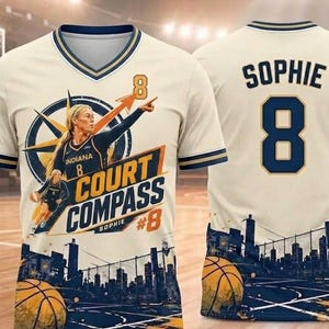 Op de afbeelding: Een crèmekleurig V-hals shirt met een basketbalspeler-afbeelding, een kompasontwerp en de tekst "COURT COMPASS" met "SOPHIE #8". De achterkant toont de naam "SOPHIE" en het nummer "8" in marineblauw, met een stadssilhouet en basketbalprint.