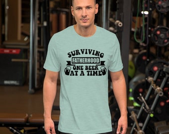 May include: A light blue t-shirt with black text that reads "SURVIVING FATHERHOOD ONE BEER AT A TIME" with a beer mug graphic on either side of the text.