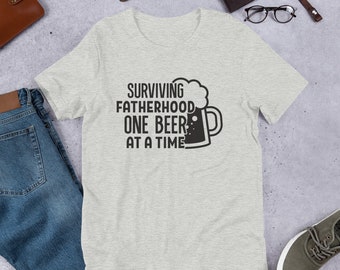 May include: A heather grey t-shirt with a black graphic of a beer mug and the text "SURVIVING FATHERHOOD ONE BEER AT A TIME".