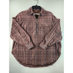 Könnte beinhalten: Ein langärmliges, braun-lila kariertes Hemd mit halbem Reißverschluss und ausgefranstem Saum. Das Hemd hat eine kleine Brusttasche und geknöpfte Manschetten. Das Hemd hängt an einem schwarzen Kleiderbügel.