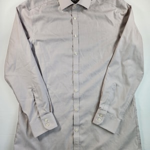 May include: A light mauve dress shirt with a subtle striped pattern. The long-sleeved shirt features a button-down front, a classic collar, and buttoned cuffs. The shirt has a label at the neck.