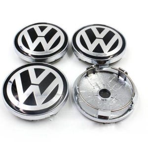 Può includere: Quattro coprimozzi Volkswagen argento e neri. I coprimozzi sono di forma ovale con un logo "VW" nero al centro. Un coprimozzo è smontato, mostrando il retro e l'anello di tenuta.