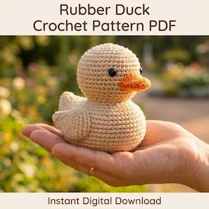 Puede incluir: Un patito de goma tejido a ganchillo, beige con pico naranja y ojos negros, se sostiene en una mano. El texto "Rubber Duck Crochet Pattern PDF" está en la parte superior y "Instant Digital Download" en la inferior. Un artículo de artesanía.