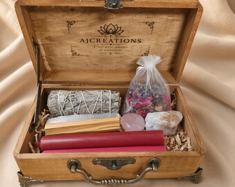 Può includere: Una scatola di legno con chiusura e maniglia in metallo contenente un fascio di salvia, un bastoncino di palo santo, un sacchetto trasparente di petali di fiori secchi, un cristallo rosa, una pietra bianca e due candele rosse. Il coperchio interno riporta il testo AJCREATIONS.
