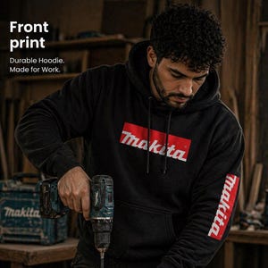 May include: Black hoodie featuring the Makita logo in red and white on the front and sleeve. The text "Front print" and "Durable Hoodie. Made for Work." are displayed above the logo. A person is wearing the hoodie while using a drill on a wooden plank. The text "FRONT PRINT HOODIE" is displayed at the bottom.