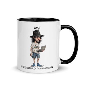May include: White ceramic mug with a black interior and handle. The mug features a cartoon illustration of a person wearing a hat and holding a laptop. Text on the mug reads "SHAX" and "NOTORIOUS LEADER OF THE BLACKHATTER BOTS."