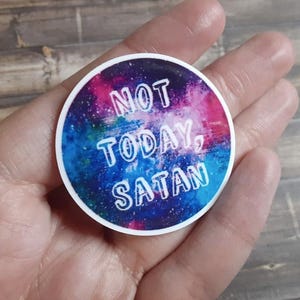 May include: A circular sticker with a galaxy-themed background featuring shades of blue, purple, and pink. The text NOT TODAY, SATAN is printed in white, bold, sans-serif capital letters across the centre of the sticker.