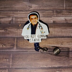 May include: A badge reel featuring a graphic of a man in a white medical coat with a stethoscope around his neck. Below the figure, the text reads YOU NOT GONNA STARVE! in black capital letters on a white background. The reel has a clear plastic strap.
