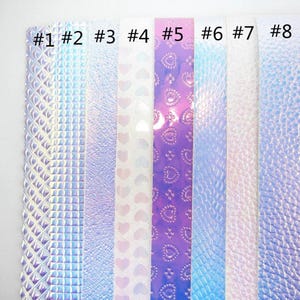 May include: Eight vertical strips of iridescent material labeled #1 through #8. The textures include diamond patterns, square grids, fine grain, heart shapes, and pebbled surfaces, all featuring a shifting color palette of blue, pink, and white.