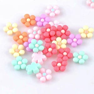May include: A collection of colorful, small flower-shaped embellishments in various shades of pink, orange, yellow, and blue. Each flower has a white center, creating a cheerful and decorative appearance. These are ideal for craft projects.