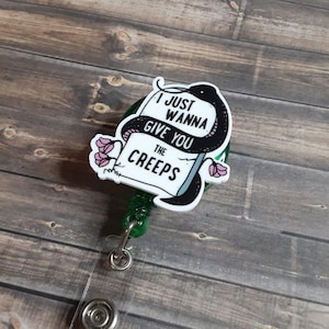 May include: A green retractable badge reel featuring a white acrylic topper with a black snake illustration. The design includes pink flowers and the black text I JUST WANNA GIVE YOU THE CREEPS. The badge reel has a metal clip and clear plastic strap.