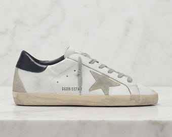 Zapatillas Golden Goose Superstar: Zapatillas casuales bajas de cuero blanco desgastado con estrellas grises.