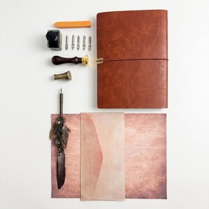 May include: A collection of vintage writing supplies, including a brown leather journal, ink, a wax seal, a feather quill pen, and stationery. The items are arranged on a white surface, with a warm, inviting color palette.