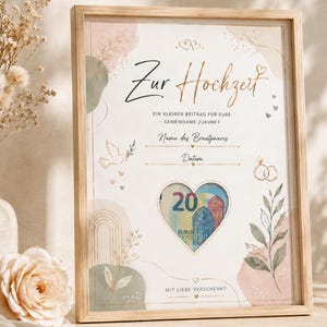 May include: A light wood framed print featuring the German text Zur Hochzeit, Ein kleiner Beitrag für eure gemeinsame Zukunft, Name des Brautpaares, Datum, and Mit Liebe verschenkt. A heart-shaped cutout displays a 20 Euro banknote inside.