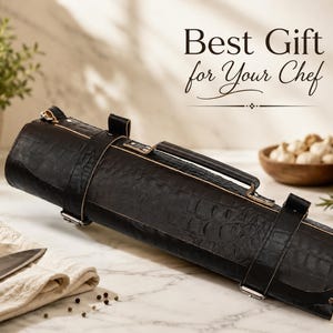 Può includere: Un rotolo di coltelli in pelle nera con manico e cinghie, esposto su una superficie di marmo. Il testo "Best Gift for Your Chef" è sopra il rotolo. Sono visibili anche un coltello, aglio e olio d'oliva.