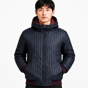 Könnte beinhalten: Eine marineblaue Steppjacke mit vertikalen Nähten, einem durchgehenden Frontreißverschluss und einer Kapuze. Die Jacke verfügt über ein dunkelweinrotes Innenfutter, passende weinrot gestreifte Rippbündchen an den Ärmeln und einen passenden Rippsaum.