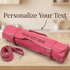 Könnte beinhalten: Eine aufgerollte, pinkfarbene Leder-Messertasche mit passendem Schultergurt. Der Text "YOUR TEXT HERE" ist auf der Vorderseite sichtbar. Die Worte "Personalize Your Text" stehen darüber.