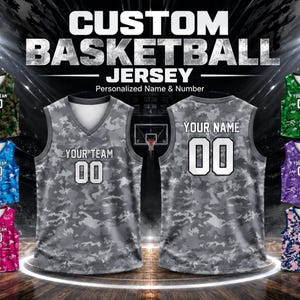 Op de afbeelding: Aangepaste basketbalshirts met gepersonaliseerde namen en nummers. De afbeelding toont verschillende shirts in verschillende camouflagepatronen, waaronder grijs, groen, blauw, roze en paars. Elk shirt heeft de tekst "YOUR TEAM" of "YOUR NAME" en het nummer "00".