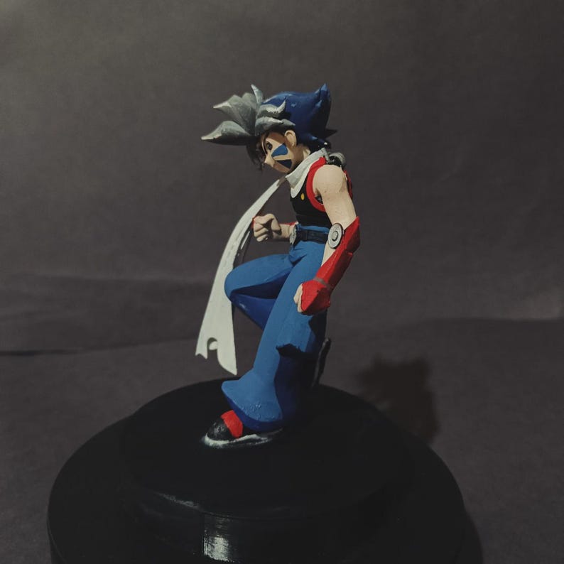 May include: A figurine of a character with blue hair and a white cape. The figure is wearing blue trousers, a red and black top, and red arm guards. The figure is posed in a dynamic stance on a black base.