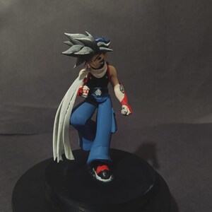 May include: A figurine of a character with spiky grey hair, wearing a black top, blue trousers, and red and white arm sleeves. The figure has a white scarf and is posed dynamically on a black base.