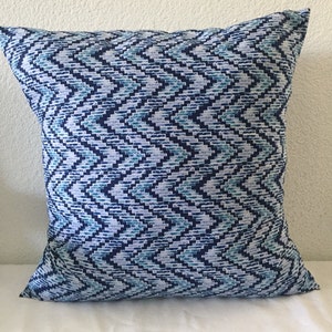 May include: Blue and white geometric patterned throw pillow. The pillow has a chevron pattern with a subtle blue and white color scheme.