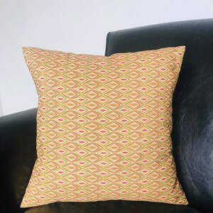 May include: A gold and red patterned throw pillow with a diamond design. The pillow is on a black leather couch.