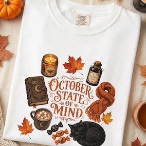 May include: A white t-shirt featuring a graphic print with the text "OCTOBER STATE OF MIND" surrounded by illustrations of a lit candle, a spell book, a bottle labeled "witches brew", a mug of cocoa, a knitted scarf, candies, and a black cat.