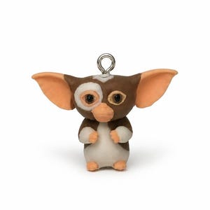 May include: A small, sculpted figurine of a creature with large, pointed ears, brown and white fur, and a light peach-colored nose and feet. The figure features a metallic silver jump ring attached to the top of its head for hanging purposes.