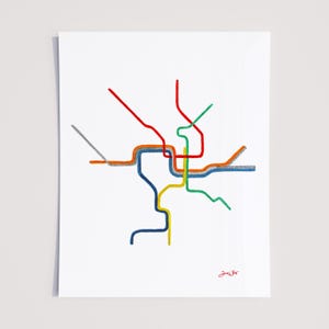 May include: A colorful abstract print featuring a map-like design with lines in red, orange, blue, green, yellow, and gray on a white background. The artwork has a minimalist style and includes a signature in the bottom right corner.