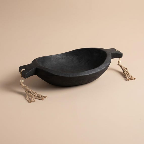 A bold hand-carved black wood bowl with rope handles — the kind of sculptural object that looks like it belongs in a design magazine, not a craft fair.