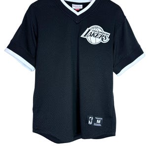 May include: A black mesh V-neck jersey with white trim on the collar and sleeves. The front features a white Los Angeles Lakers logo and a Mitchell & Ness tag with size M at the bottom. The jersey is displayed on a wooden hanger against a white background.