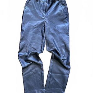Può includere: Pantaloni blu navy metallizzati con gamba dritta. I pantaloni hanno un classico stile a cinque tasche con chiusura con bottone e cerniera. Il tessuto ha una lucentezza sottile e le cuciture sono visibili in un colore più chiaro.