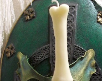 May include: A white candle in a clear glass candle holder. The candle is on a table with a brown and white rope and a green and gold background.