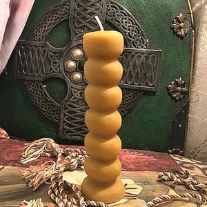 May include: A tall, yellow beeswax candle with a textured, ridged design. The candle is sitting on a brown and white patterned surface.